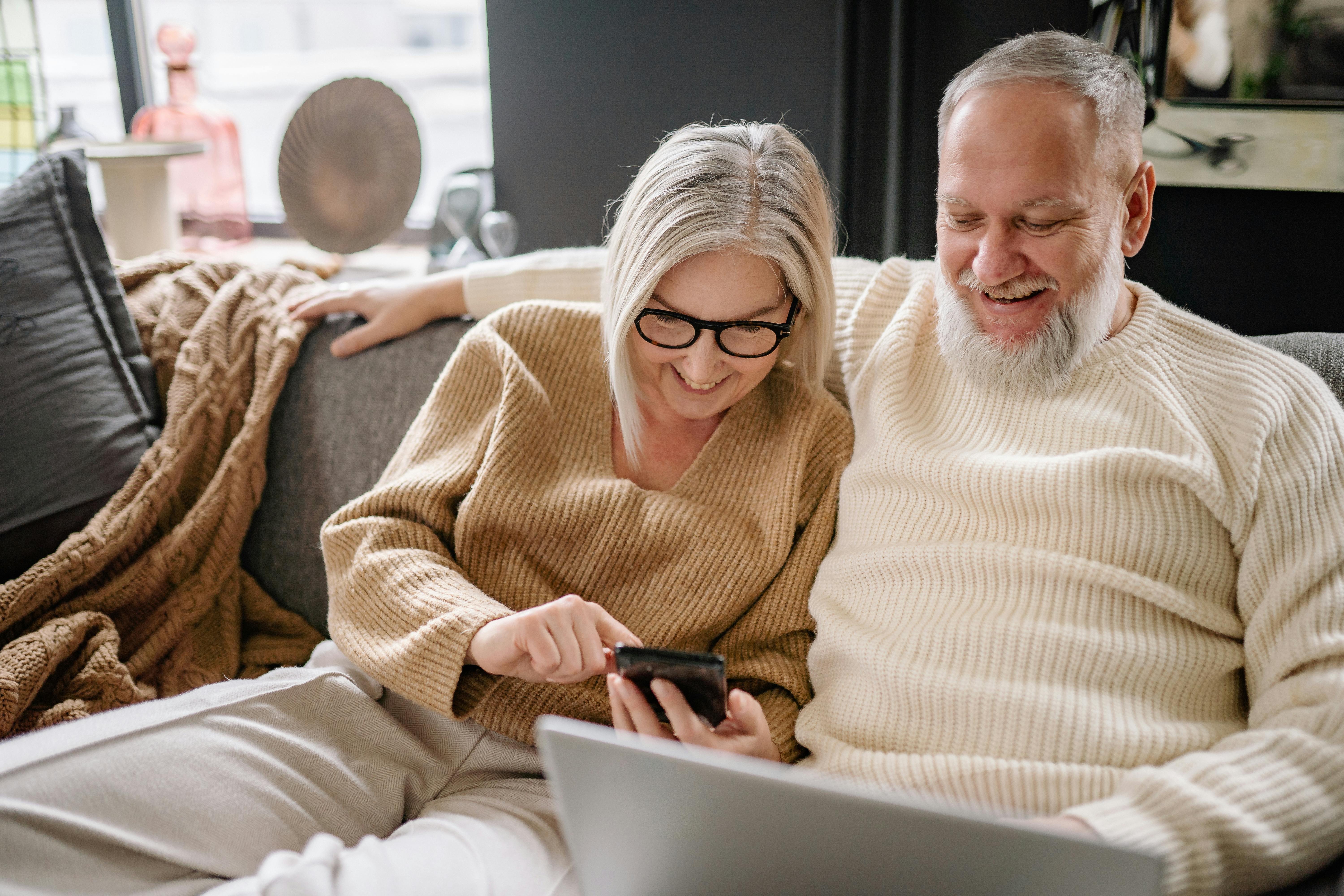 Couple smiling and browsing devices together on the couch